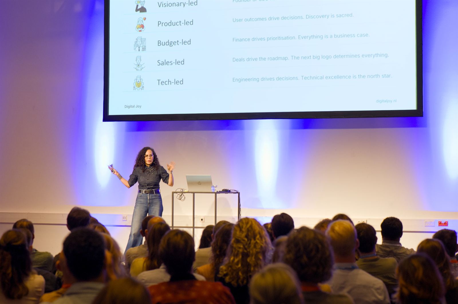 Joy Adamson speaking to a full room in front of a slide on visionary-, product-, budget-, sales- and tech-led organisations